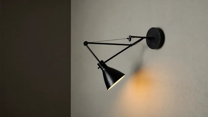 Aplică neagră reglabilă care proiectează un con de lumină pe tencuială.